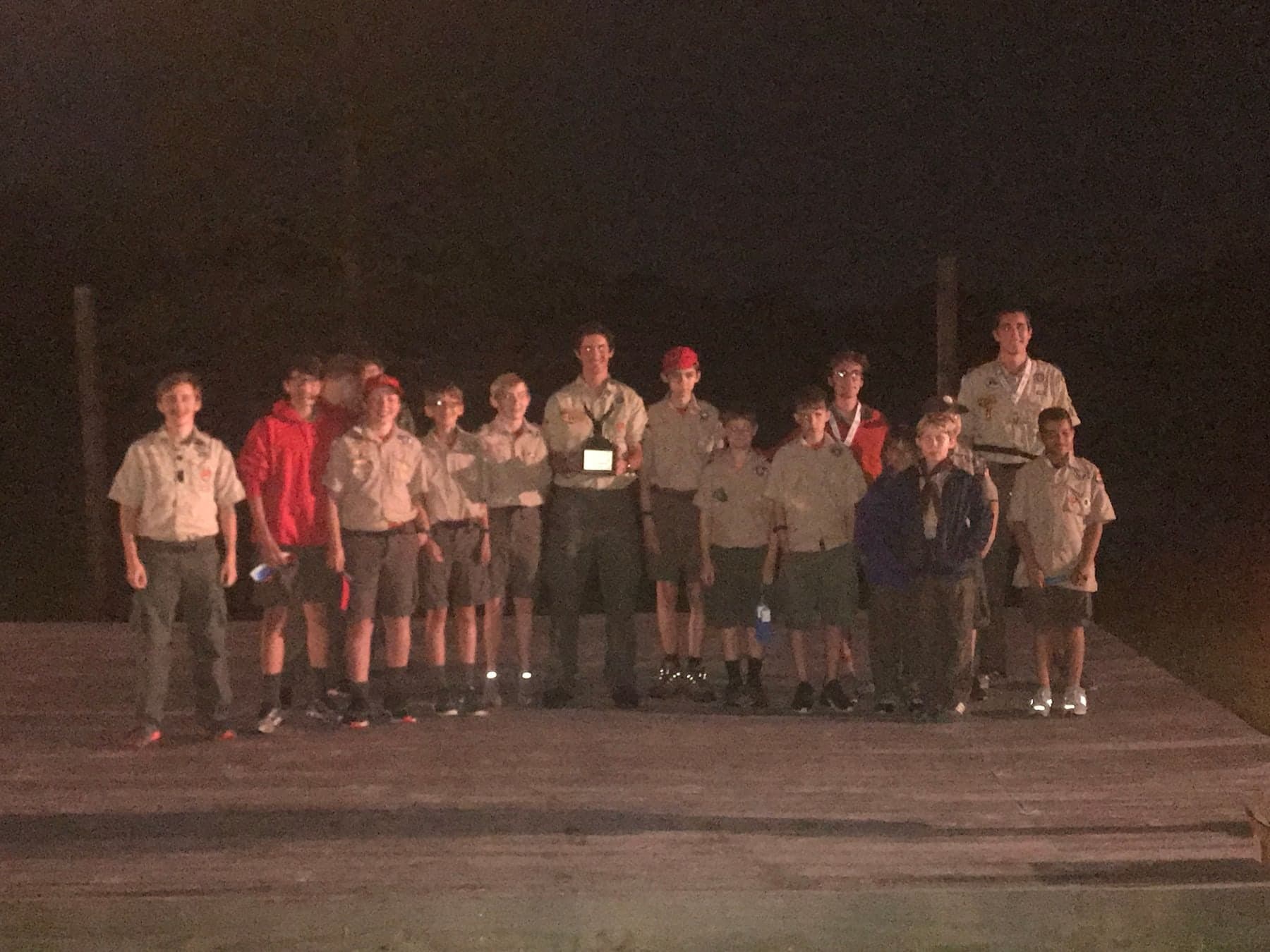 Colin Raby, center, holding the Most Outstanding Troop trophy with the Scouts of Troop 50 on the camporee stage at night