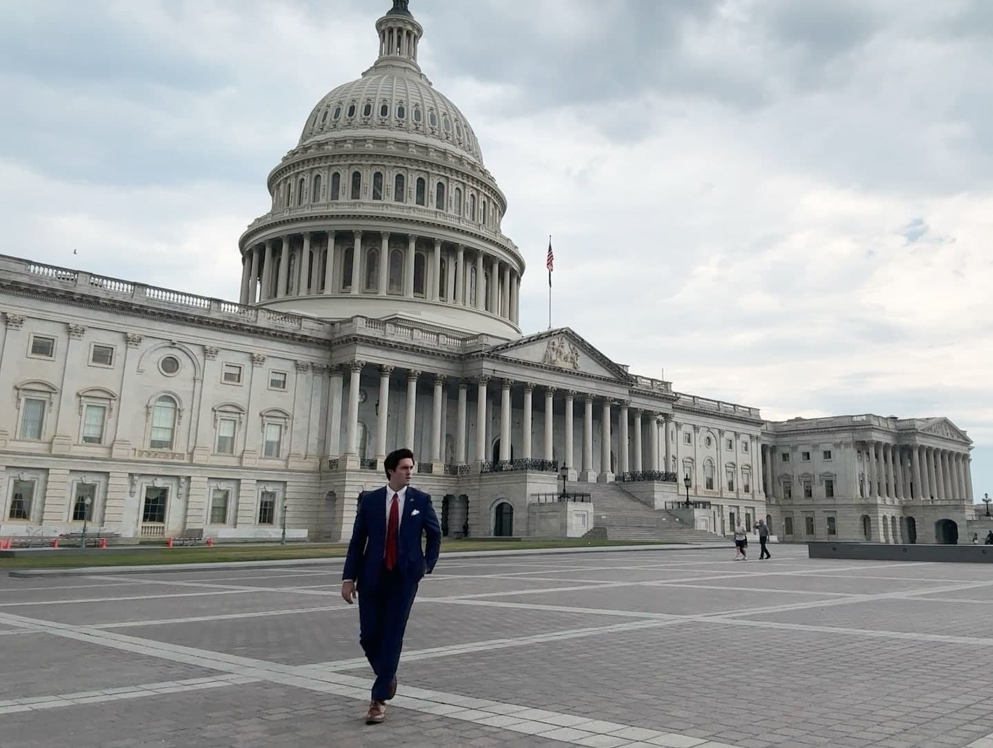 Colin Raby walking across the East Front plaza of the U.S. Capitol in a navy suit and red tie