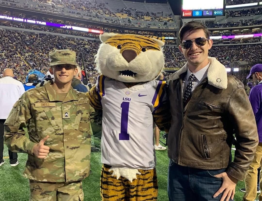 Colin Raby in a leather flight jacket with Mike the Tiger and an Air Force ROTC cadet on the field at Tiger Stadium