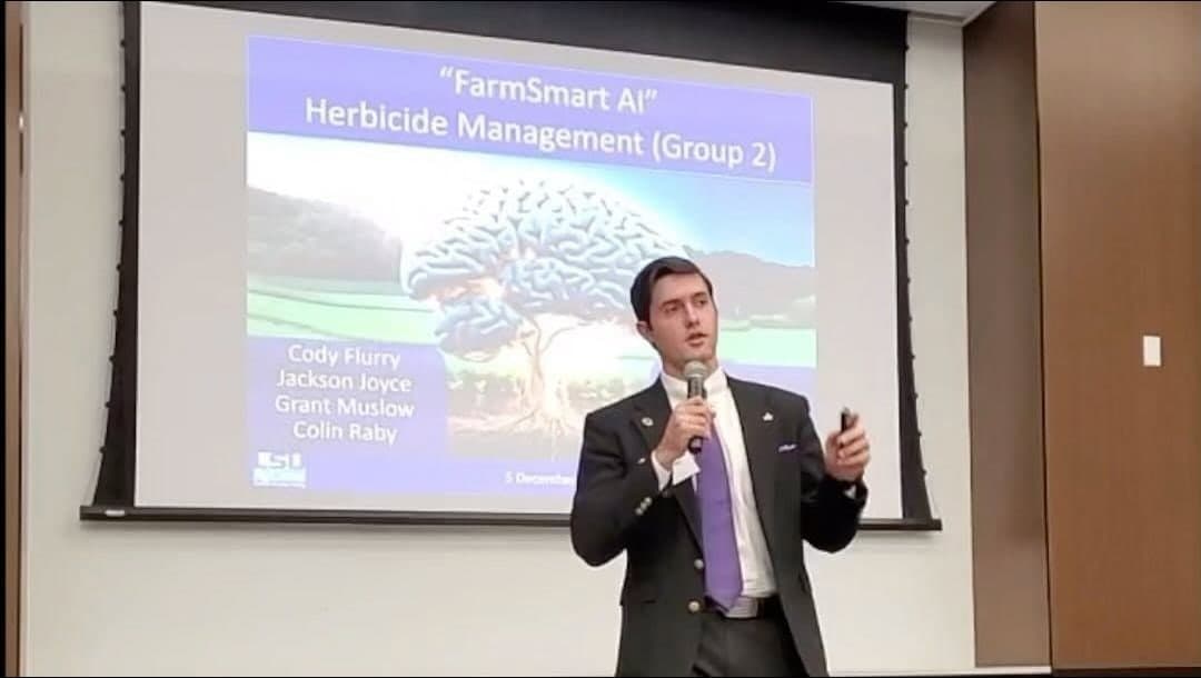 Colin Raby presenting in front of a slide reading “FarmSmart AI, Herbicide Management (Group 2)” with the names Cody Flurry, Jackson Joyce, Grant Muslow and Colin Raby