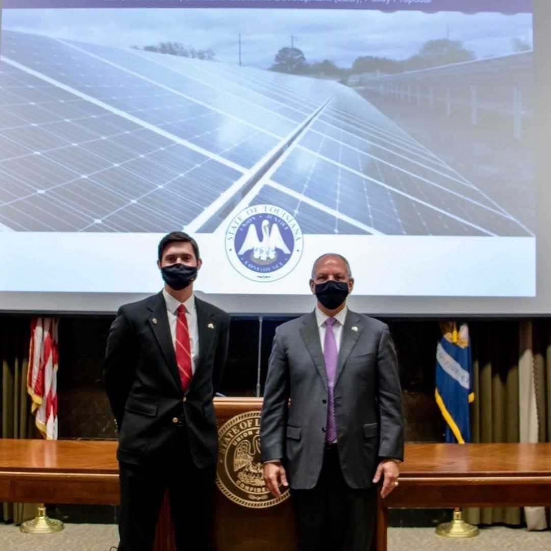 Colin Raby and Gov. John Bel Edwards at the podium in front of a slide of a solar farm