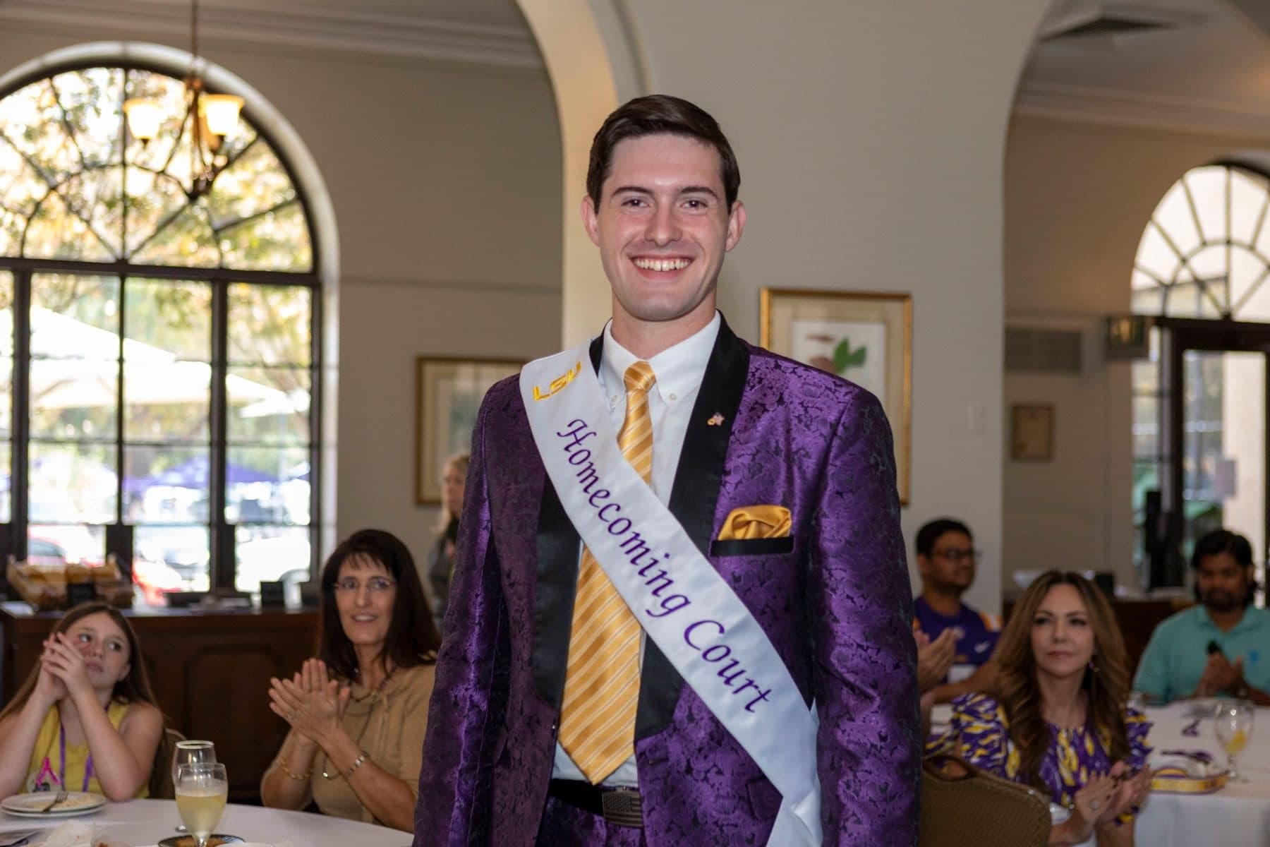 Colin Raby in a purple suit wearing a "Homecoming Court" sash at the court luncheon