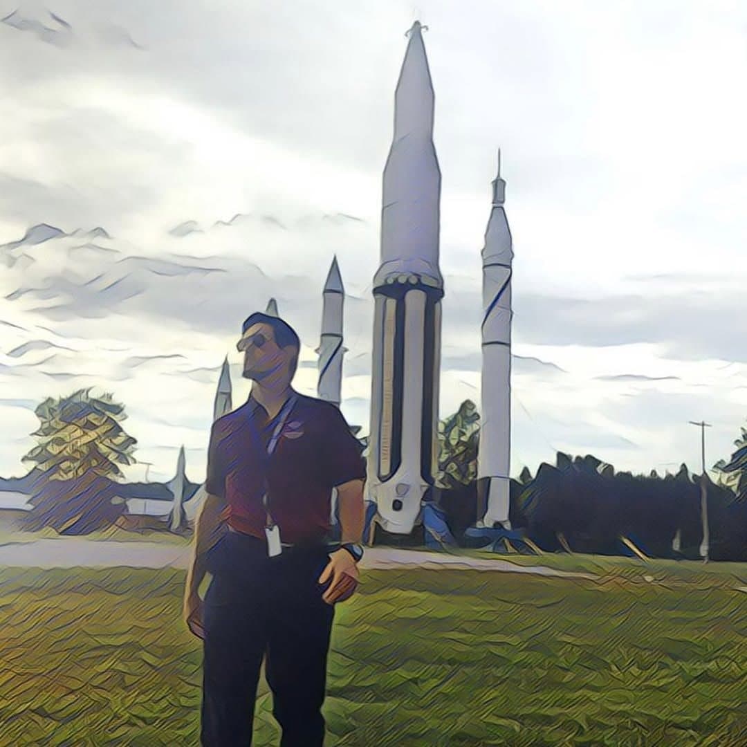 Colin Raby standing beneath historic rockets in Huntsville, in a stylized photo