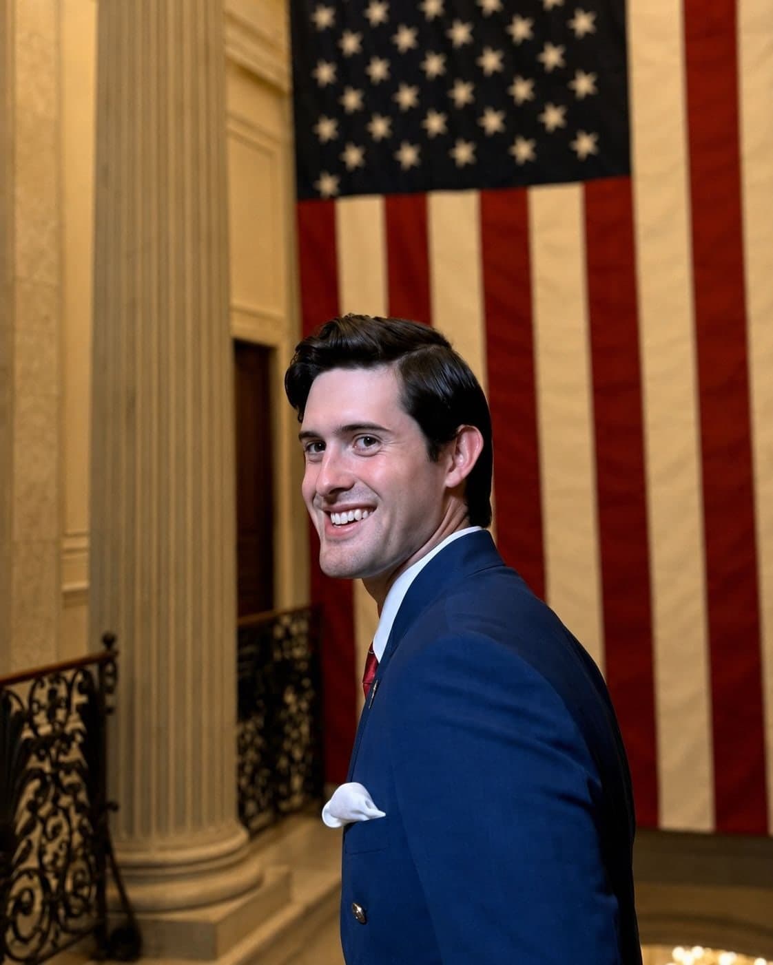 Colin Raby in a navy suit on a marble staircase on Capitol Hill, a large American flag behind him