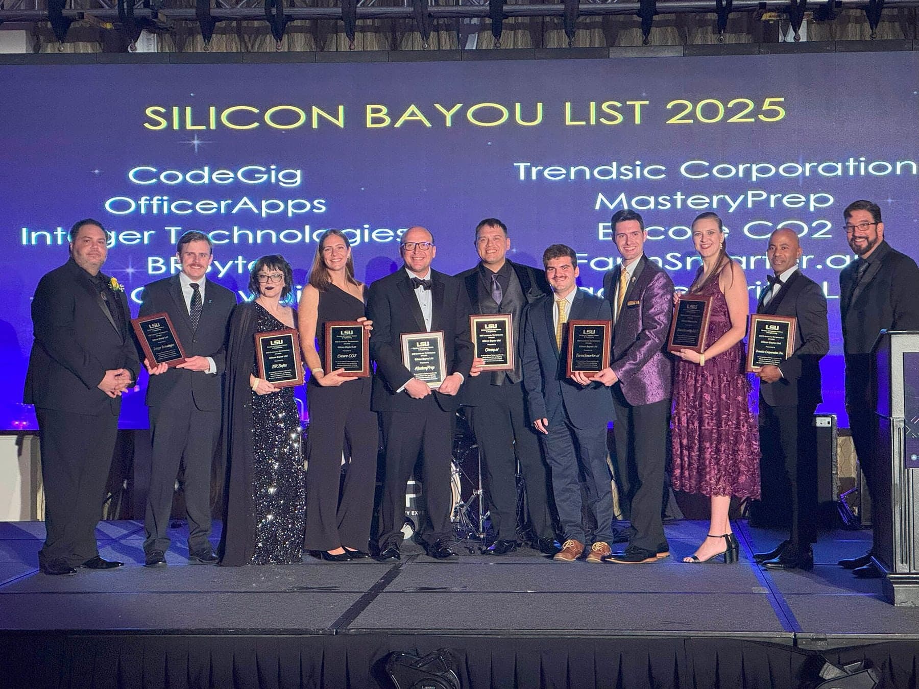 The 2025 Silicon Bayou List honorees on stage at LSU's gala holding plaques, with Colin Raby in a purple jacket beside the FarmSmarter.ai plaque, under a screen listing the honorees