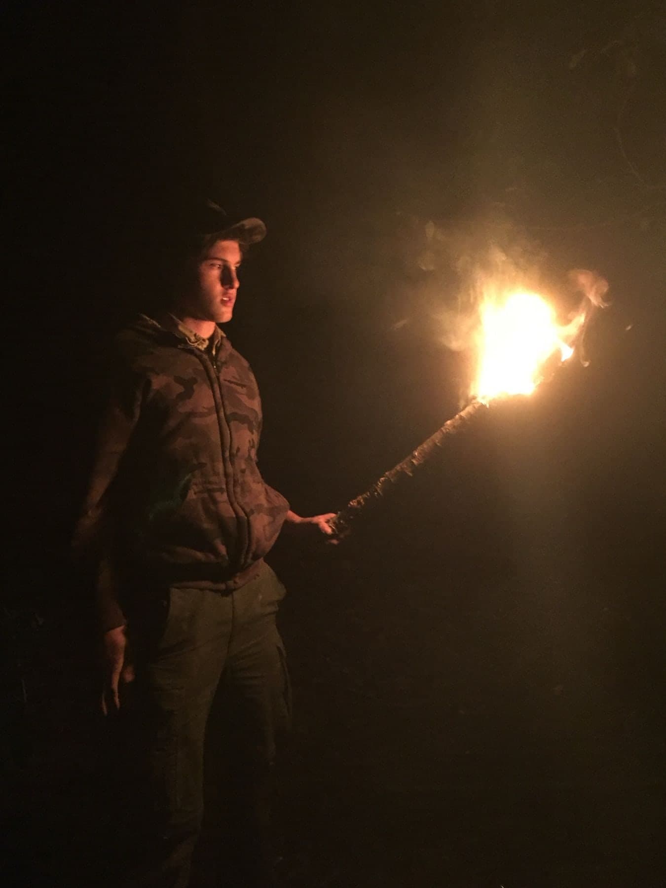 Colin Raby at night in a camouflage jacket and cap, holding a burning torch