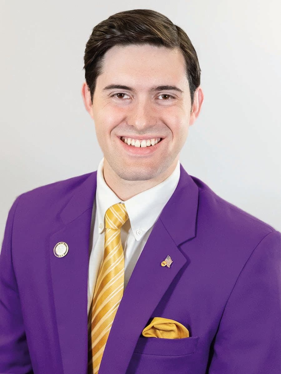 Colin Raby's official Tiger Twelve portrait, in a purple blazer and gold striped tie
