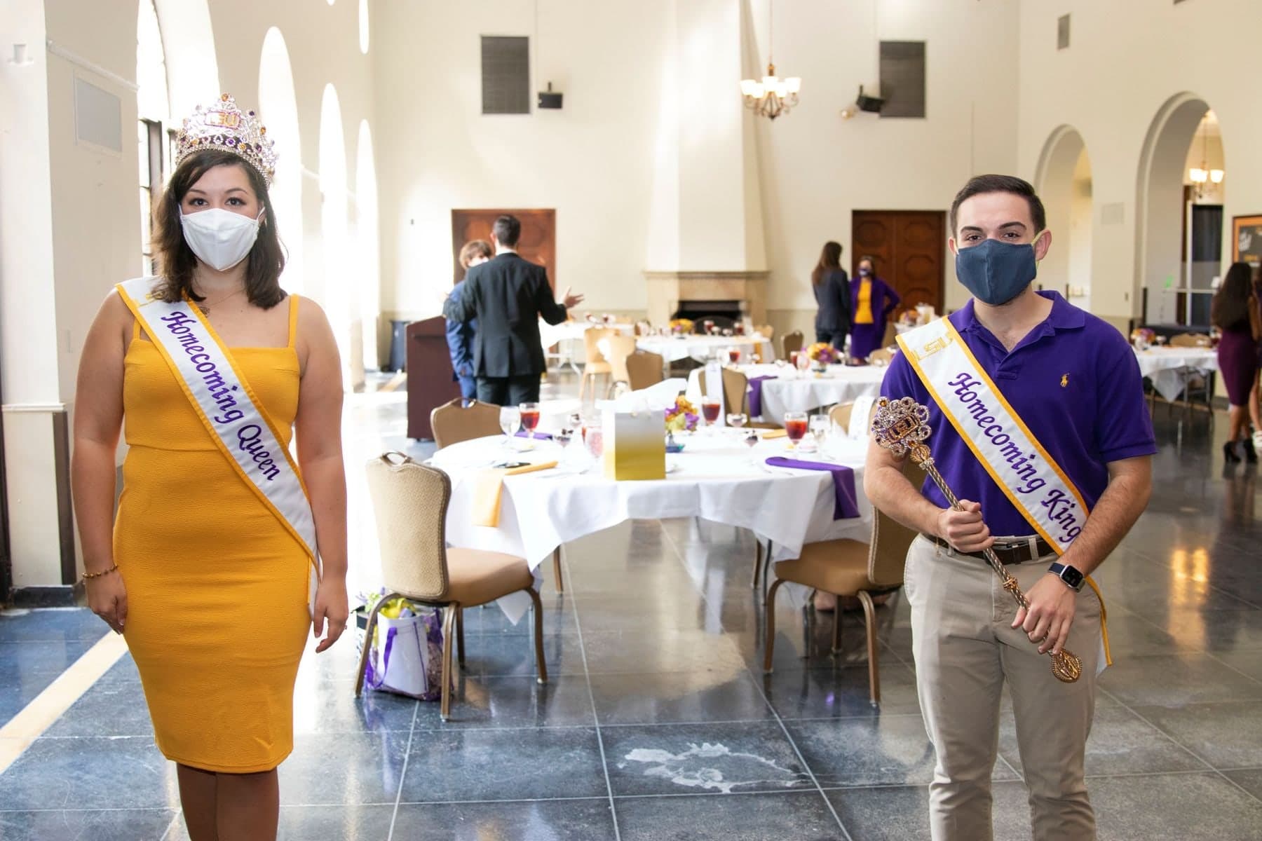 Colin Raby in a purple blazer and Homecoming sash, masked, beside a fellow court member in yellow at the luncheon