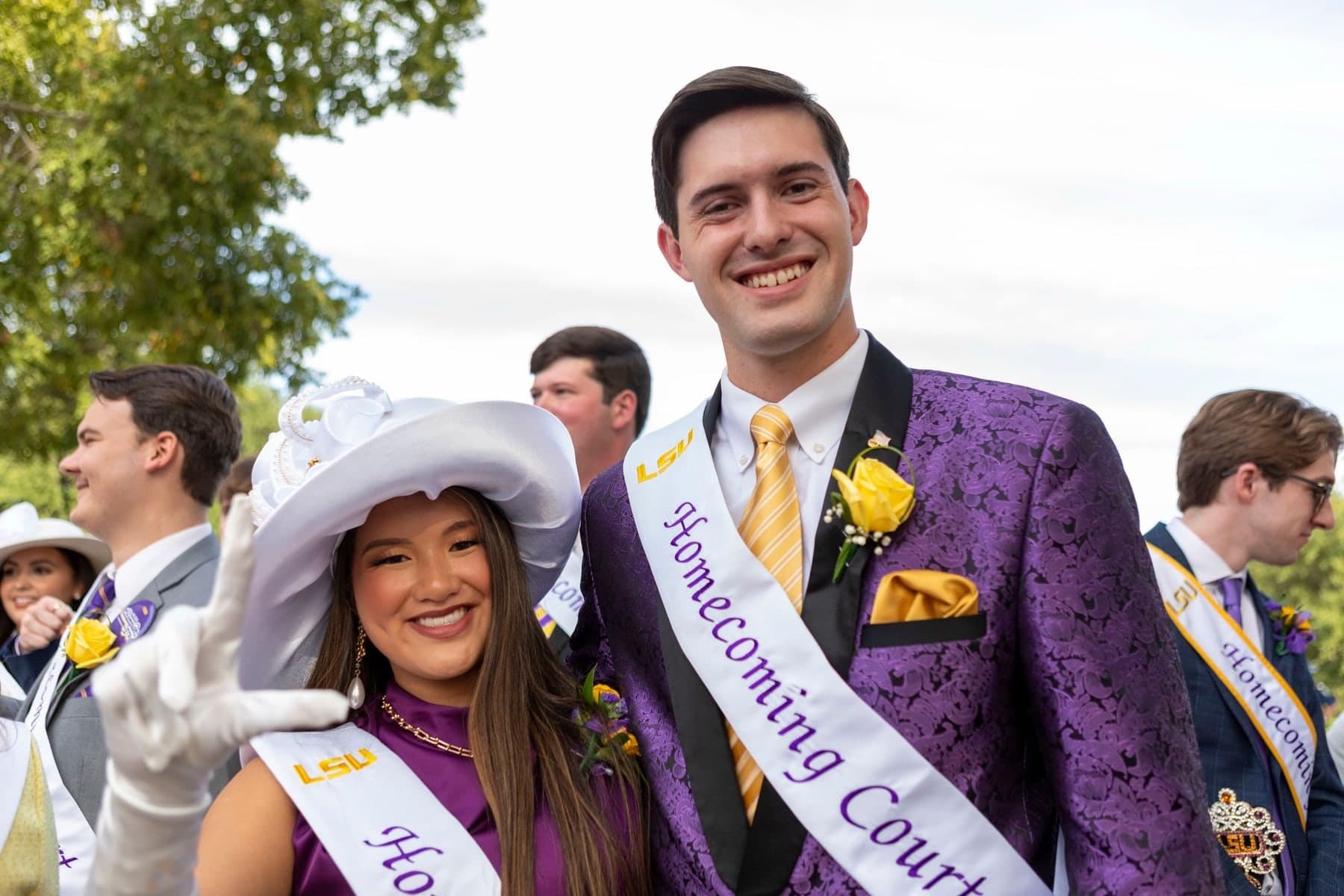 Colin Raby smiling in a purple suit and Homecoming Court sash beside a fellow court member in a white hat