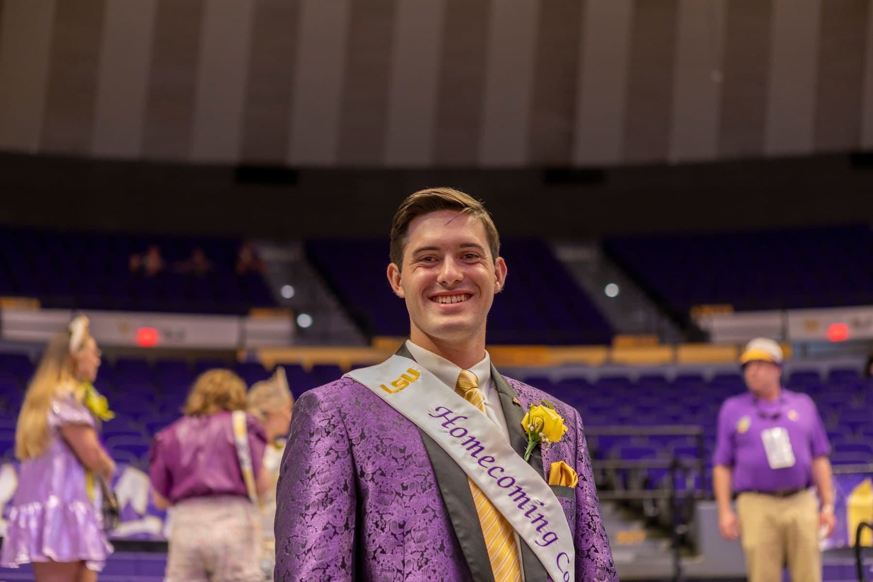 Colin Raby in a purple suit and Homecoming Court sash inside an arena with purple seats