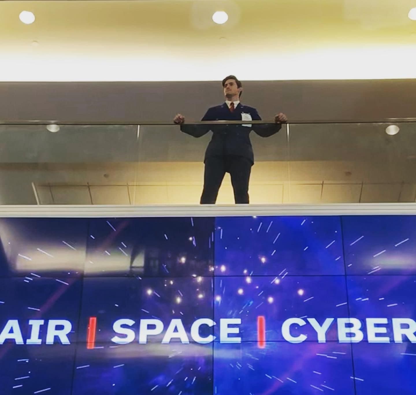 Colin Raby standing at a balcony railing above a screen reading “Air | Space | Cyber”
